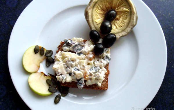 Artischocke, Weintrauben, Birne, Apfel, getrocknete Aprikosen, Kürbiskerne mit Frischkäse dekoriert auf einer Scheibe Vollkornbrot