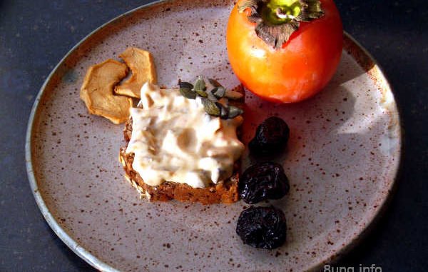 Khaki, Trockenobst, Kürbiskerne mit Frischkäse, angerichtet auf einem Keramikteller