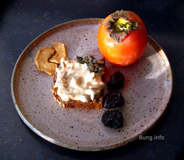 Khaki, Trockenobst, Kürbiskerne mit Frischkäse, angerichtet auf einem Keramikteller