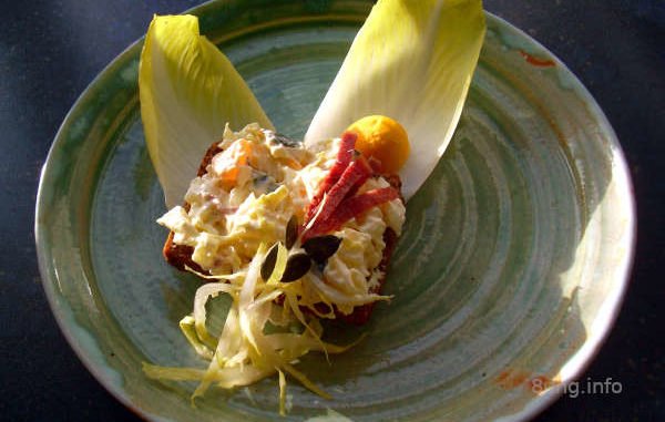 Chicorée, Zunge, Ei, Mandarine, Apfel, Rosinen, Kürbiskerne mit Frischkäse, angerichtet auf einem Vollkornbrot