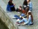 Mädchen sitzen auf den Pflastersteinen am Fluss
