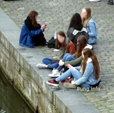 Mädchen sitzen auf den Pflastersteinen am Fluss