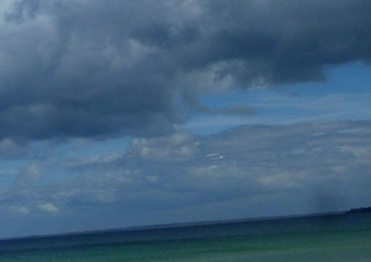 einsame Frau am Strand, viele Wolken, Wasser grün bis blau
