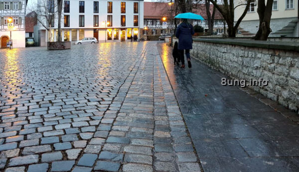 regennasses Kopfsteinpflaster, Frau mit bleuem Schirm