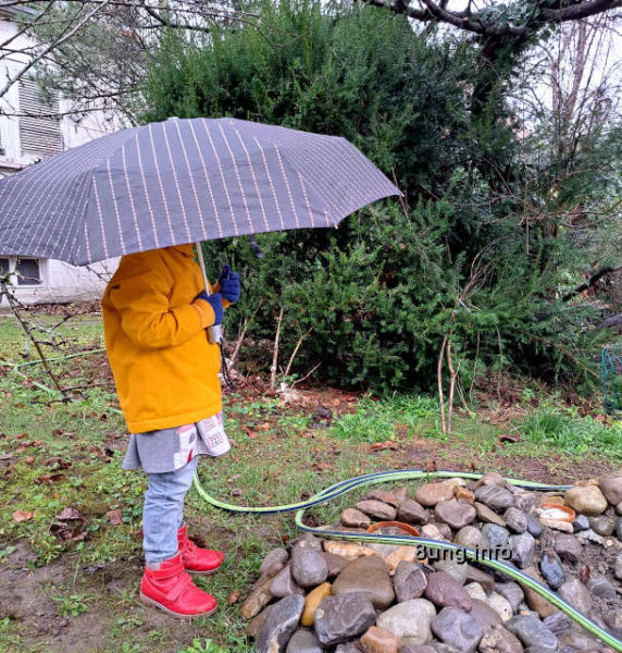 Kind mit Regenschirm und gelber Jacke