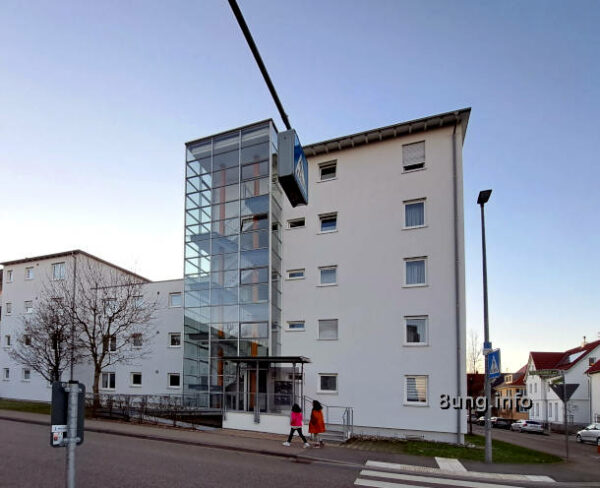 graues Haus, rote Mäntel von Spaziergängerinnen
