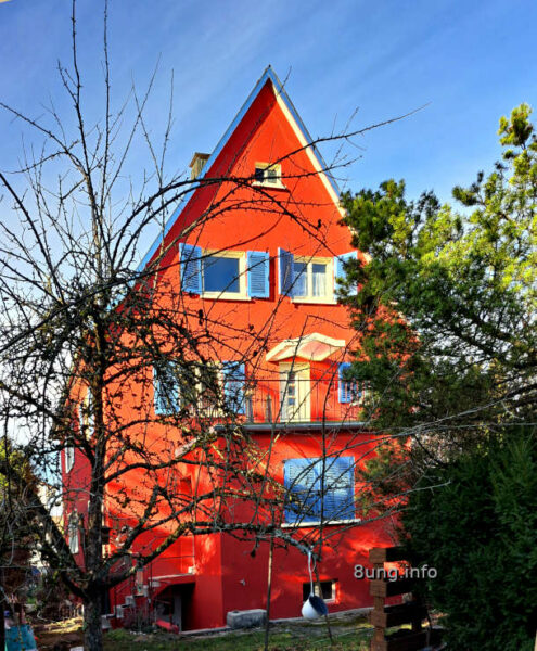 rotes Haus mit blauen Fensterläden im Sonnenschein, blauer Himmel