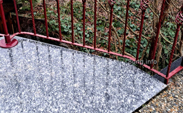 Regen auf der Steinplatte, Schatten von einem rostroten Geländer