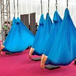 Foto zum Download: Yoga zur Entspannung: Riesige blaue Laken, an zwei Zipfeln befestigt, hängen von der Decke. Darin liegt eine nicht sichtbare Person. Ihre Hände baumeln entspannt nach außen. Gespenstisch bis lustig.