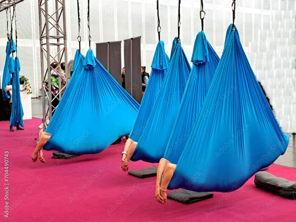 Foto zum Download: Yoga zur Entspannung: Riesige blaue Laken, an zwei Zipfeln befestigt, hängen von der Decke. Darin liegt eine nicht sichtbare Person. Ihre Hände baumeln entspannt nach außen. Gespenstisch bis lustig.
