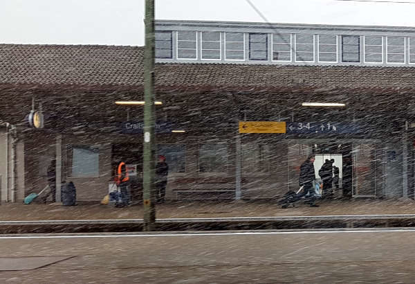 Schneegestöber auf dem Bahnhof, Reisende mit Koffern