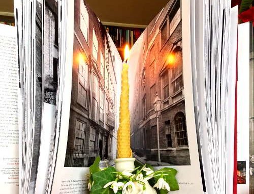 Schneeglöckchen im Kerzenhalter mit Fotobuch über Häuserschluchten im Hintergrund