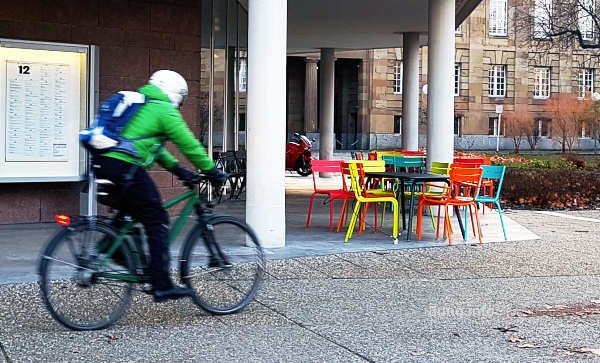 Radfahrer mit grüner Jacke fährt an bunten Stühlen vorbei